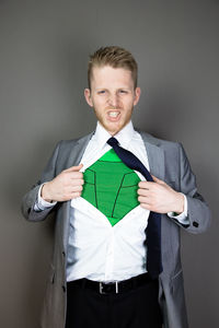 Portrait of businessman showing superhero costume underneath suit against gray background