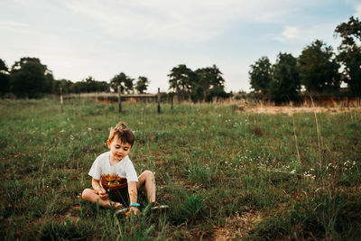 Young boy sitting in an open field picking flowers