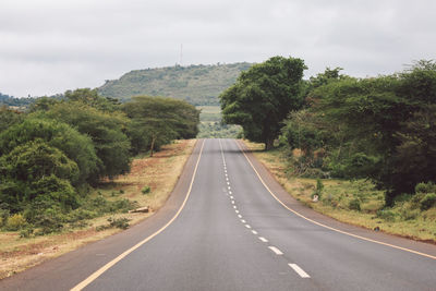 Empty road amidst trees against sky