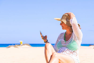 Side view of woman using phone while sitting at beach