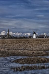 Distance shot of windmill on landscape against clouds