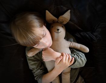 Directly above shot of boy embracing stuffed toy while lying on bed