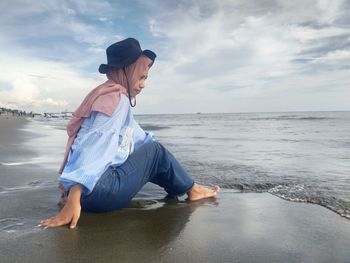 Young woman sitting on beach against sky