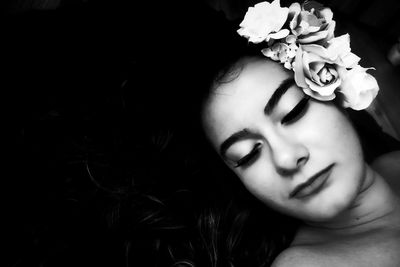 Close-up of young woman wearing flowers on hair against black background