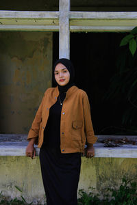 Portrait of a young woman standing against wall