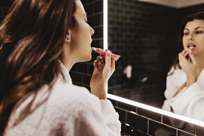 Mid adult woman looking in mirror while applying lipstick at hotel