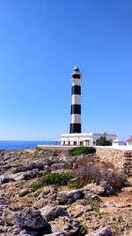 Lighthouse by sea against clear blue sky