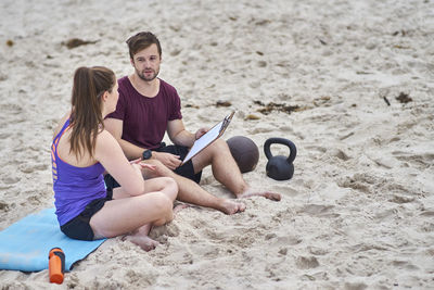 Fitness instructor assisting woman in exercising at beach