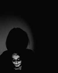 Portrait of young woman standing against black wall