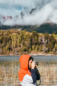 Side view of woman photographing while standing by lake