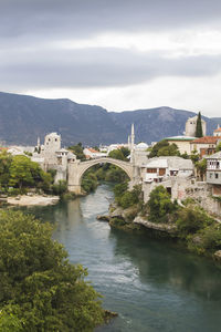 Arch bridge over river by buildings against sky