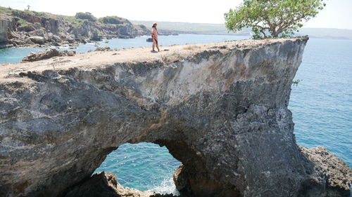 Side view of mid adult woman standing on cliff by sea during sunny day