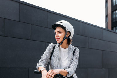 Young woman looking away while standing against wall