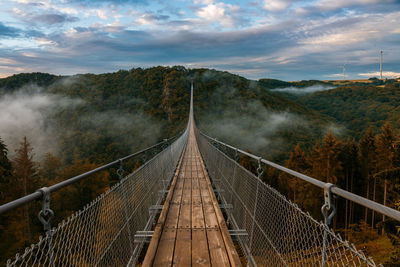 Footbridge amidst trees against sky