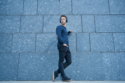 Modern man in casual clothes leaning against a wall listening to music