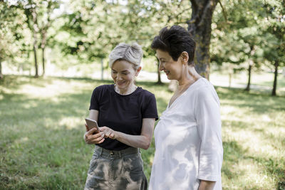 Woman using mobile phone while standing by friend at park