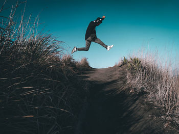 Side view of young man jumping against sky