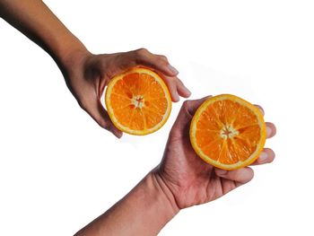 Cropped image of hand holding orange fruit against white background