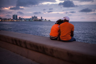 Rear view of man and woman sitting against sea at dusk