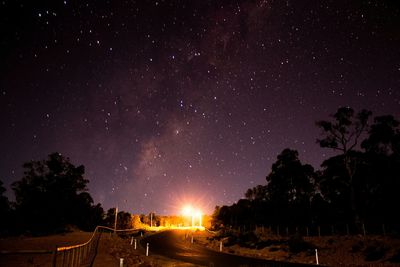 Paved road under starry night sky illuminated at end