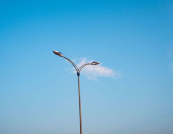 Low angle view of bird perching on street light against clear blue sky