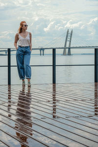 Full length of woman standing on pier over sea against cloudy sky