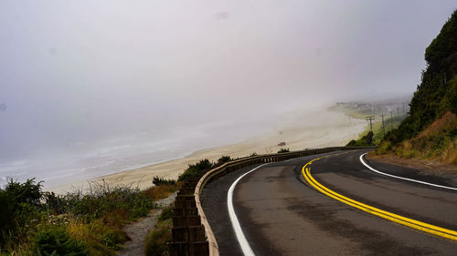 Empty road amidst trees against sky