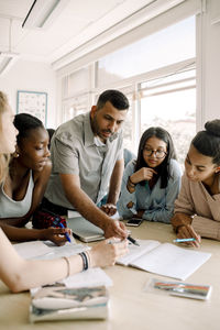 Professor teaching female teenagers while standing by table in classroom