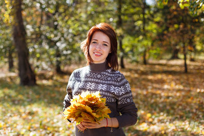 Beautiful young woman with light brown hair in sweater on background of foliage