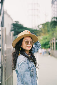 Portrait of woman wearing hat standing against city in background