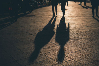 Low section of silhouette people walking on street during sunset