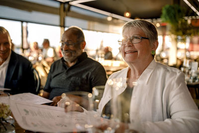 Smiling senior woman wearing eyeglasses sitting with menu card by men in restaurant