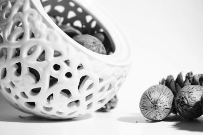 Close-up of walnuts and pine cone by container against white background