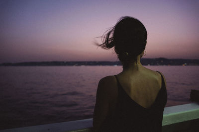 Side view of woman looking at sea against sky during sunset