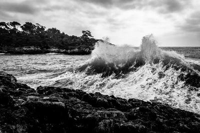 Waves splashing on rocks by sea against sky