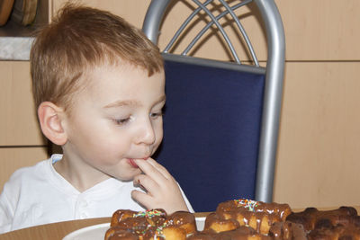 Cute boy eating cookies on table at home