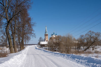 Snow covered road amidst trees against clear sky