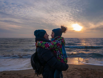 Mother and daughter in warm clothes on empty beach with blue sea sunset sky. south scenic landscape 