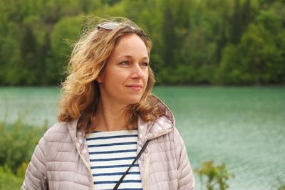Portrait of smiling young woman standing against lake