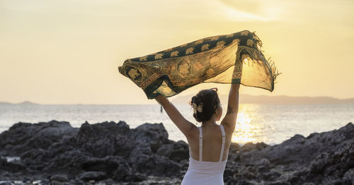 Woman tourist raising hands with sunset at beach on vacation trip. female relaxing with common cloth 