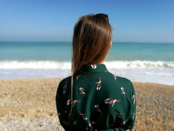 Rear view of woman standing at beach against sky