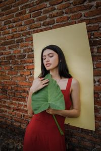 Young woman standing against brick wall