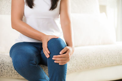 Midsection of woman suffering from knee pain while sitting at home