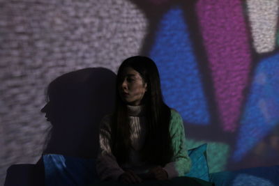 Woman sitting against wall in dark room