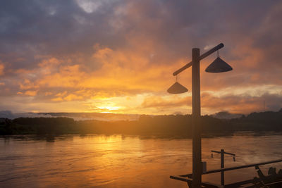 Silhouette street light by lake against sky during sunset