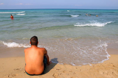 Rear view of shirtless man looking at sea against sky