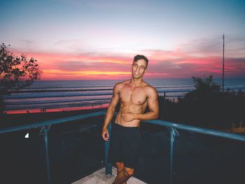 Portrait of shirtless man standing by railing against sea