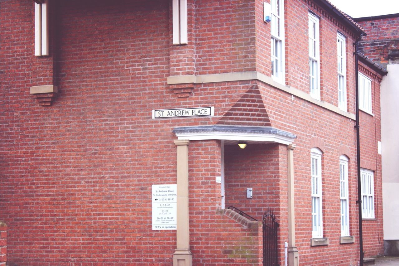 architecture, building exterior, built structure, brick wall, window, text, red, building, communication, western script, low angle view, city, residential building, wall - building feature, residential structure, day, brick, outdoors, no people, sign