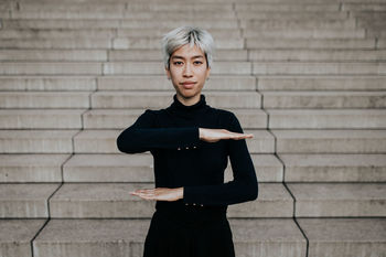 Portrait of smiling woman gesturing equal sign while standing on staircase