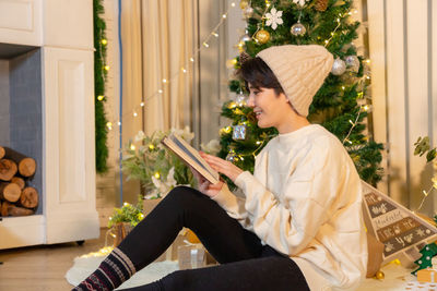 Side view of young woman using mobile phone while sitting on sofa at home